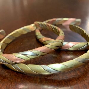 May include: Three braided metal bracelets with a copper, silver, and gold finish. The bracelets are stacked on top of each other.