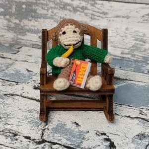 May include: A crocheted monkey doll sitting in a wooden rocking chair, holding a banana and a book titled "DAHL".