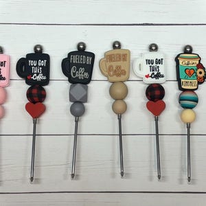 Peut inclure: Ensemble de sept bâtonnets à café sur le thème du café avec différents motifs et couleurs. Les motifs comprennent des tasses à café avec des textes tels que "You Got This Coffee" et "Fueled by Coffee". Les bâtonnets sont en acier inoxydable et ont une variété de perles colorées.