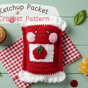 May include: A red and white crocheted ketchup packet with a smiling face and a tomato applique. The image includes a crocheted hamburger, fries, and a red and white checkered napkin. Text reads "Ketchup Packet Crochet Pattern."