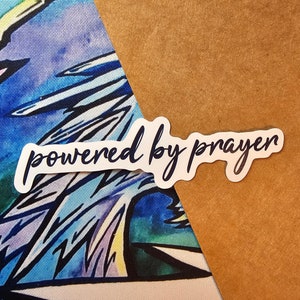 May include: White sticker with the text "powered by prayer" in black cursive lettering on a brown background.
