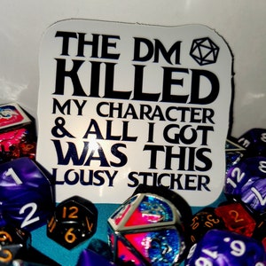 May include: A white sticker with black text that reads "The DM Killed My Character & All I Got Was This Lousy Sticker". A black and white dice icon is in the upper right corner of the sticker. The sticker is surrounded by colorful dice.