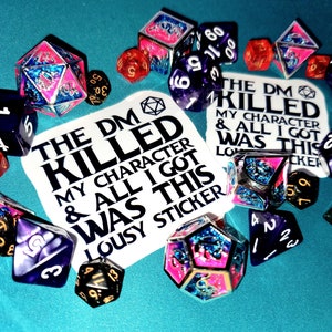 May include: A white sticker with the text "The DM Killed My Character & All I Got Was This Lousy Sticker" surrounded by colorful dice with glitter and metallic accents.