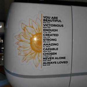 May include: A yellow sunflower sticker with inspirational text and bible verses. The text reads "You are beautiful, victorious, enough, created, strong, amazing, capable, chosen, never alone, always loved".