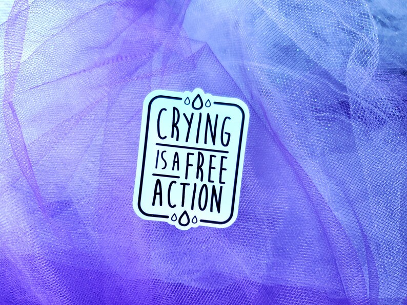 May include: A white sticker with black text on a purple and blue tulle background. The text reads "Crying is a free action".