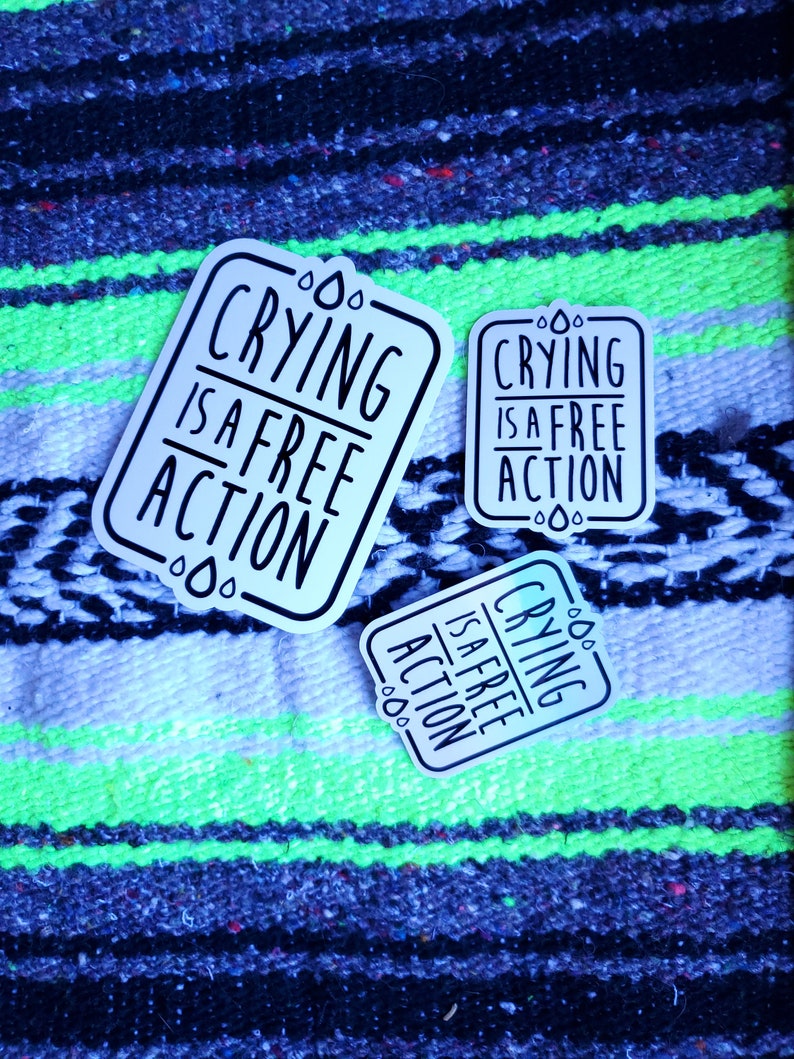 May include: Three white stickers with black text that reads "Crying is a free action" on a colorful striped background.