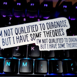 May include: Two white stickers with black text on a black keyboard. The text on the stickers reads "I'm not qualified to diagnose but I have some theories."