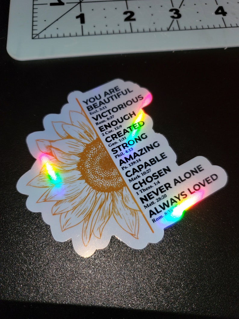 May include: A sticker featuring a sunflower design with a rainbow iridescent finish. The sticker includes inspirational text with bible verses, such as "You are beautiful", "Victorious", "Enough", "Created", "Strong", "Amazing", "Capable", "Chosen", "Never Alone", and "Always Loved".