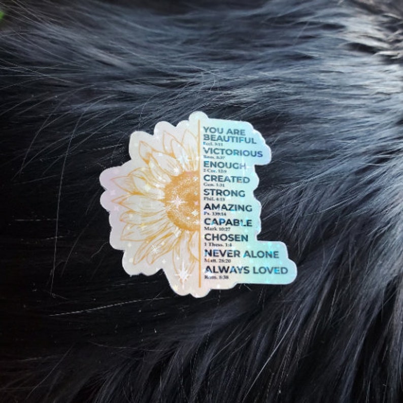 May include: A sticker featuring a sunflower design and inspirational text. The text reads "You are beautiful, victorious, enough, created, strong, amazing, capable, chosen, never alone, always loved." The sticker has a holographic finish.