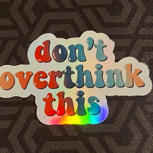 May include: A holographic sticker with the text "don't overthink this" in a rainbow color scheme.
