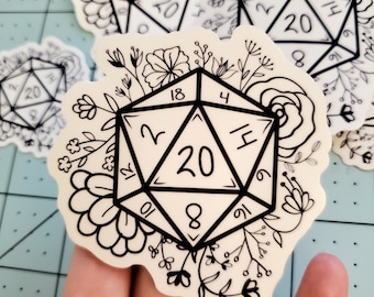 May include: A white sticker with a black outline of a twenty-sided die with floral designs around it. The die has numbers 2, 4, 6, 8, 10, 12, 18, and 20 on it.