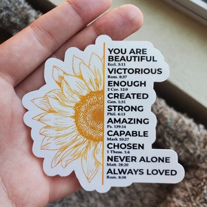 May include: A white sticker featuring a yellow sunflower design and inspirational text. The text reads "You are Beautiful, Victorious, Enough, Created, Strong, Amazing, Capable, Chosen, Never Alone, Always Loved" with Bible verses listed below each phrase.