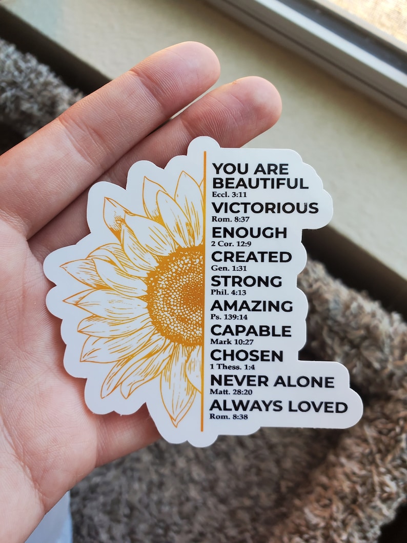 May include: A white sticker featuring a yellow sunflower design and inspirational text. The text reads "You are Beautiful, Victorious, Enough, Created, Strong, Amazing, Capable, Chosen, Never Alone, Always Loved" with Bible verses listed below each phrase.