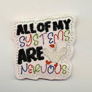 May include: A white glittery fabric patch featuring the embroidered black text ALL OF MY SYSTEMS ARE NERVOUS. The words are accented with colorful thread in blue, red, and green. A small white goose with an orange beak is stitched near the text.