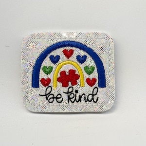 May include: A square, glittery patch with a rainbow design and the words "be kind." The rainbow features a blue arch, a yellow arch, and red, green, and blue hearts. A red puzzle piece is in the center of the rainbow.