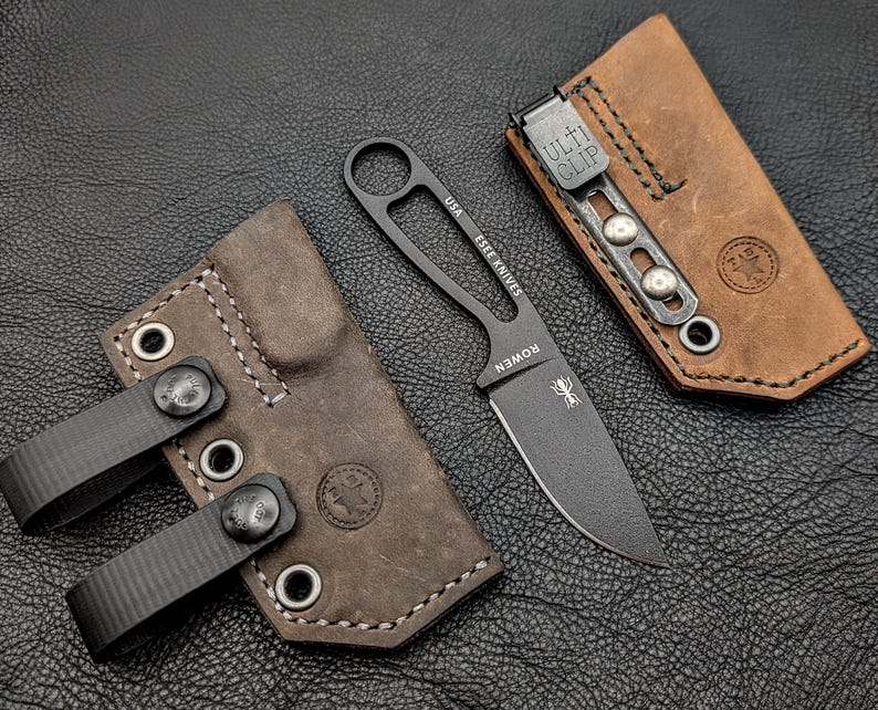 May include: A black fixed-blade knife with a leather sheath and a brown leather sheath with a metal clip. The knife has the text "USA ESEE KNIVES" and "ROWEN" on the blade. The sheaths are brown with black stitching.