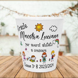 Può includere: Un vaso in ceramica bianca con un design colorato che presenta un sole, una nuvola, un arcobaleno e bambini. Il testo sul vaso recita "Grazie Maestra Luciana Per averci aiutato a crescere Classe 3^ B 2023/2024".