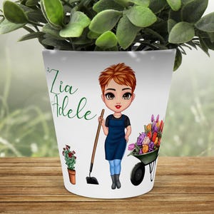 Può includere: Vaso di fiori in ceramica bianca con un'illustrazione di un giardiniere con una zappa, una carriola di fiori e il testo "Zia Adele". È raffigurato anche un piccolo vaso con una pianta.