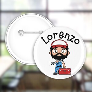 Può includere: Un bottone bianco con un'immagine di un uomo con la barba che indossa un cappello rosso e una tuta blu che tiene una chiave inglese e una cassetta degli attrezzi rossa. Il testo "Lorenzo" è stampato in nero sopra l'immagine.