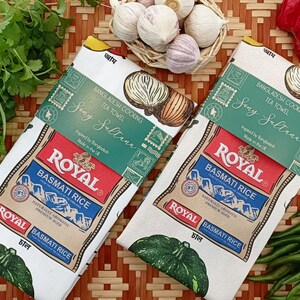 May include: Two white tea towels with a design featuring a bag of Royal Basmati Rice, text, and a green leaf. The towels are labeled "Bangladesh Cooking Tea Towel" and "Sony Sultana". Fresh vegetables surround the towels.