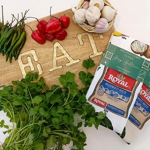 May include: A wooden cutting board with the word "EAT" in gold letters, surrounded by fresh ingredients. Green chilies, red peppers, cilantro, garlic, and two "Royal Basmati Rice" packages are visible.