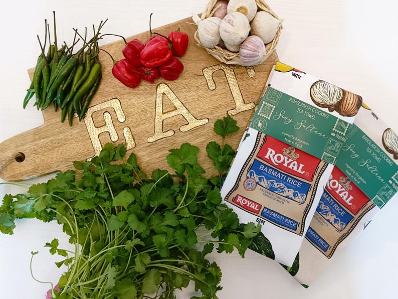 May include: A wooden cutting board with the word "EAT" in gold letters, surrounded by fresh ingredients. Green chilies, red peppers, cilantro, garlic, and two "Royal Basmati Rice" packages are visible.