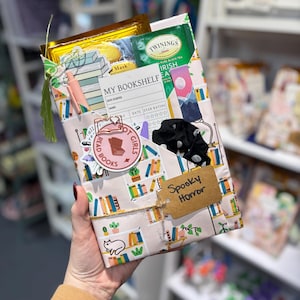 May include: A pink and white gift wrapped with a bookshelf pattern. The gift is tied with twine and has a brown tag that says "Spooky Horror".