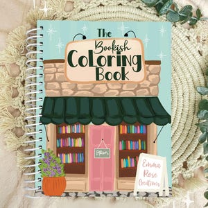 May include: A spiral-bound coloring book titled "The Bookish Coloring Book" with an illustration of a bookstore. The cover features a teal background with a bookstore facade, a pink door, and a sign that says "Open". A sign reads "Emma Rose Creations".