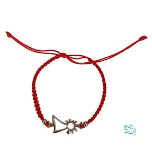 Puede incluir: Pulsera de cordón trenzado rojo con un dije plateado. El dije presenta un diseño estilizado de sol y flecha. La pulsera tiene nudos corredizos ajustables. Fondo blanco.