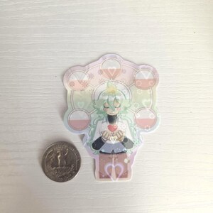 May include: A colorful sticker featuring an anime-style character with green hair, holding a red heart. The sticker has a decorative border with floral and geometric elements. A quarter is next to the sticker for size comparison.