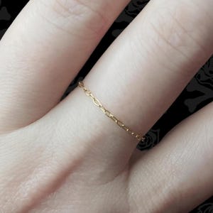 May include: A delicate gold chain ring. The ring is thin and simple, with a delicate chain design.