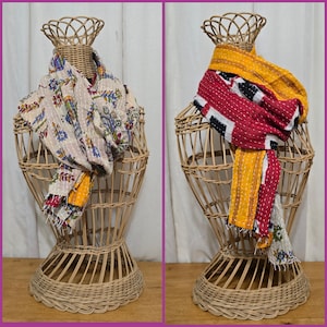 May include: Two decorative scarves displayed on wicker stands. One scarf features a floral pattern with blue, green, and yellow accents. The other scarf has a red, black, and white design with yellow and white stripes.