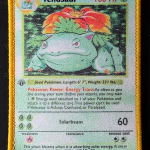May include: A Venusaur Pokémon card patch with a green and orange design. The card features the text "Venusaur" and "100 HP". The patch has a yellow border and includes the text "Stage 2".