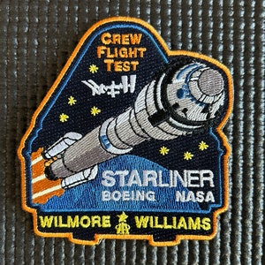 May include: A blue and orange embroidered patch with a rocket ship and the text "Crew Flight Test #1 Starliner Boeing NASA Wilmore Williams".