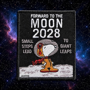 Könnte beinhalten: Ein rechteckiger, schwarzer Stickaufnäher mit einem weißen Cartoon-Hund in einem orangefarbenen Raumanzug und Helm auf einer grauen Mondoberfläche. Der Text lautet FORWARD TO THE MOON 2028, SMALL STEPS LEAD TO GIANT LEAPS in weißer Stickerei.