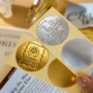 May include: Close-up of gold and silver foil stickers. The gold sticker features a horseshoe design with the text "LUCKY OMEN STAMP". The silver sticker has floral accents and the text "With love Audrey Owenson".