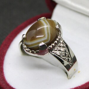 May include: A silver ring with a brown and white agate stone set in a decorative silver band.