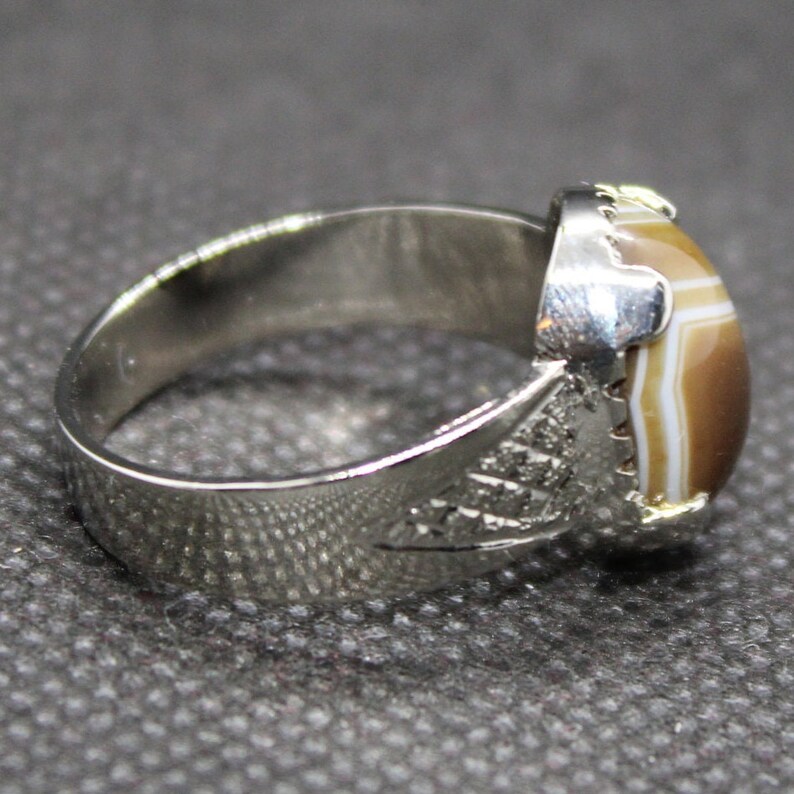 May include: A silver ring with a brown and white agate stone set in the center. The band of the ring is decorated with an intricate design.