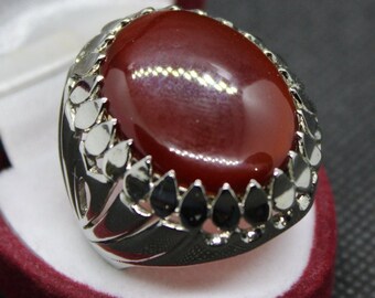 May include: A silver ring with a large, oval-shaped, red carnelian gemstone set in a decorative, silver setting.