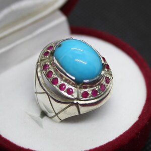 May include: A silver ring with a large oval turquoise stone surrounded by a ring of small red stones.