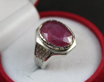 May include: A silver ring with a large, oval-shaped ruby gemstone set in a bezel setting. The ring has a textured band.