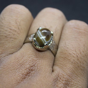 May include: A silver ring with a brown and white agate stone set in a claw setting.