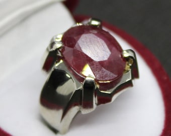 May include: A silver ring with a large, oval-shaped ruby gemstone. The ruby is a deep red color and has a faceted cut.