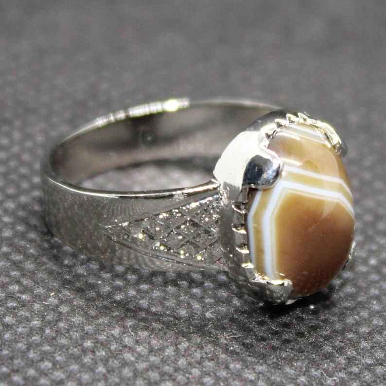 May include: A silver ring with a brown and white agate stone. The stone is set in a silver bezel and the ring band has a decorative pattern.