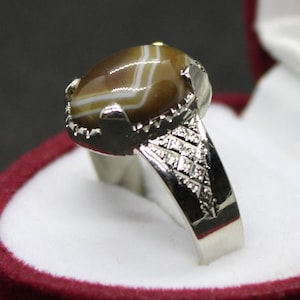 May include: A silver ring with a brown and white agate stone. The ring has a detailed design on the band.