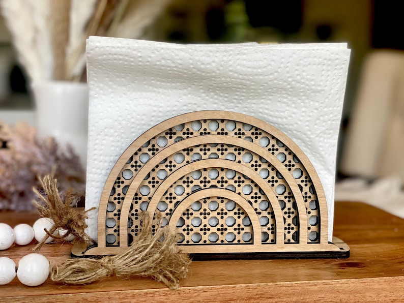 May include: Wooden napkin holder with a geometric design in the shape of a rainbow arch. The holder is made of natural wood and has a rustic look.