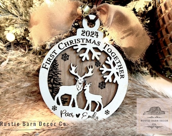 May include: White wooden Christmas ornament with a brown wood center. The ornament features a deer couple, snowflakes, and the text "First Christmas Together 2024". The names "Paor" and "Emily" are written at the bottom.