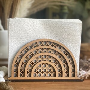 May include: Wooden napkin holder with a geometric design resembling a rainbow. The holder is made of natural wood and has a light brown color.