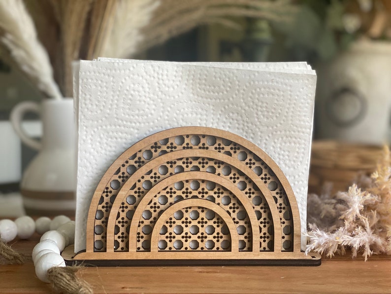 May include: Wooden napkin holder with a geometric design resembling a rainbow. The holder is made of natural wood and has a light brown color.
