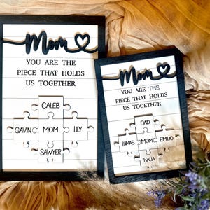 May include: Two framed wood signs with the text "Mom You are the piece that holds us together" and a heart. Each sign has a puzzle piece design with names on each piece.